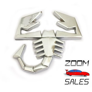May include: Silver metal scorpion emblem with a detailed design. The scorpion is facing right with its tail curled up. The emblem is a popular car accessory.