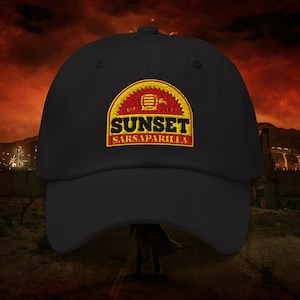 May include: Black baseball cap with a Sunset Sarsaparilla logo embroidered on the front. The logo features a red and yellow design with the text "Sunset" and "Sarsaparilla" in a bold font. The cap has a curved brim and an adjustable strap.