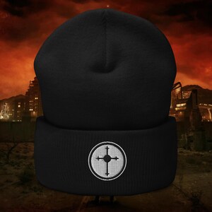 May include: Black beanie with a white embroidered emblem featuring a cross within a circle. The hat is made of a soft, knitted material. The background shows a dystopian cityscape with a red and orange sky.