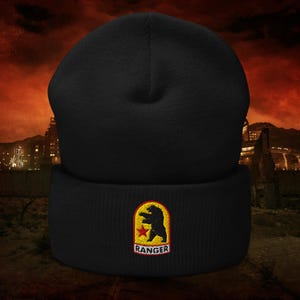 May include: Black beanie with a folded brim. The beanie features a patch with a bear silhouette, a red star, and the word "RANGER" in a rectangular design. The background shows a city skyline and a fiery sky.