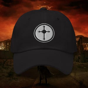 May include: Black baseball cap with a white embroidered emblem featuring a cross design within a circle. The cap has a curved brim and a structured crown. The background shows a cityscape with a red and orange sky.