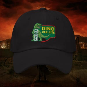 May include: Black baseball cap featuring an embroidered patch with a green dinosaur and the words "Dino Dee-Lite Motel" in green and yellow. The cap has a curved brim and a classic six-panel design.