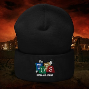 May include: Black beanie with embroidered text "The Tops Hotel and Casino" in colorful letters. The beanie is a warm, comfortable accessory, perfect for cold weather. The design features a retro aesthetic.