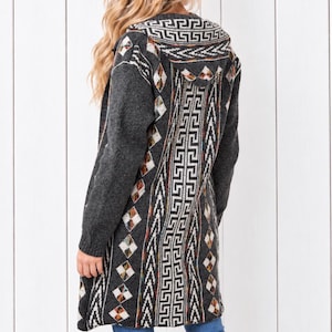 May include: A long-sleeved, charcoal gray knit cardigan featuring a hood and a prominent geometric pattern in white, black, and orange. The design includes vertical bands of Greek key motifs and diamond shapes running down the back and hood.