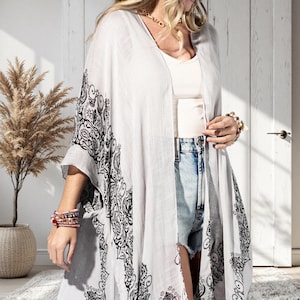 May include: A light gray kimono with black paisley-style patterns along the edges. The open-front design features wide sleeves and a flowing silhouette. The kimono is paired with denim shorts and a white top, creating a casual, layered look.