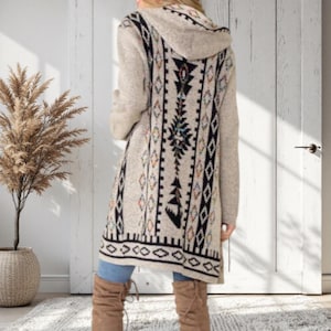 May include: A beige hooded cardigan with a geometric pattern in black, white, and colorful accents. The long sweater features a tribal-inspired design on the back and sleeves. The cardigan is knee-length and has a relaxed fit.