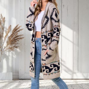 May include: A long, hooded cardigan in a beige and black geometric pattern. The open-front sweater has pockets and is worn over a white top and blue jeans. The cardigan's design features black shapes and colorful accents.