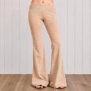 May include: High-waisted flare pants in a solid light tan color. These pants feature a fitted waist and hip area that transitions into a wide, flared leg silhouette. The fabric has a smooth, matte texture throughout the entire garment.