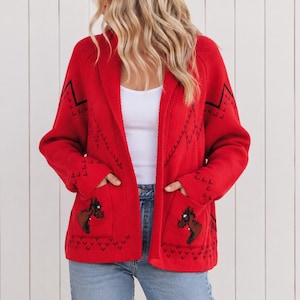 May include: A bright red open-front knit cardigan featuring long sleeves, two front patch pockets, and a black geometric pattern along the hem and sleeves. Each pocket displays a small, dark brown horse head graphic with black details.