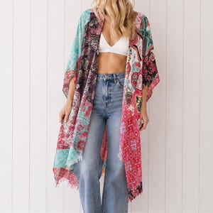 May include: A long, open-front kimono featuring a vibrant patchwork design with various floral and paisley patterns in shades of bright pink, turquoise, black, and white. The garment has wide, loose sleeves and a frayed hemline along the bottom edge.