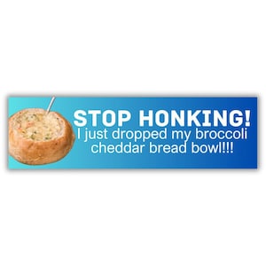 May include: A bumper sticker with a blue gradient background and white text that reads "STOP HONKING! I just dropped my broccoli cheddar bread bowl!!!" A bread bowl filled with soup is on the left.