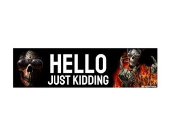 May include: Black rectangular sticker with the words "HELLO JUST KIDDING" in white. The sticker features a skull wearing sunglasses on the left and a skull engulfed in flames on the right.
