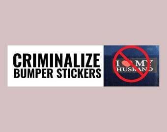 May include: A bumper sticker with the text "CRIMINALIZE BUMPER STICKERS" in bold black letters. To the right, a blue background with a sticker that says "I ❤️ MY HUSBAND" with a red circle and slash over it.