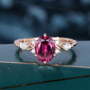 May include: Rose gold ring with an oval-cut, deep pink gemstone at its centre. The ring is embellished with smaller, clear gemstones and decorative features on the band. A classic and elegant piece of jewellery.