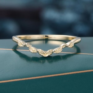 Puede incluir: Una banda de boda curvada de color dorado con un delicado diseño de hojas.