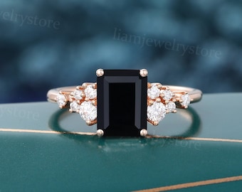 Könnte beinhalten: Ein Verlobungsring aus Roségold mit einem schwarzen Smaragdschliff-Edelstein und einem Halo aus kleineren Diamanten.
