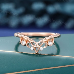 Könnte beinhalten: Ein Ring aus Roségold mit einem keltischen Knotendesign und kleinen, klaren Steinen. Der Ring liegt auf einer grünen Oberfläche.