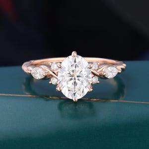 May include: A rose gold ring featuring a large oval-cut center stone flanked by two smaller marquise-cut stones and several tiny round accent stones. The band has a twisted, textured design that leads up to the central cluster of clear gemstones.