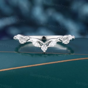 May include: A V-shaped silver-toned ring featuring a central round-cut stone flanked by marquise-cut stones and leaf-shaped metal accents along the band. The design incorporates small clear stones set into the metal leaves, creating a symmetrical arrangement.