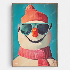 May include: A framed print featuring a snowman with sunglasses, a carrot nose, and a red hat and scarf. The snowman has a black smiling mouth and is set against a light blue background. The artwork has a vintage, retro style.