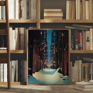 May include: A framed print of a snow-covered city alleyway at night, with string lights and tall buildings. The artwork is displayed in a wooden frame, set against a backdrop of bookshelves filled with books.