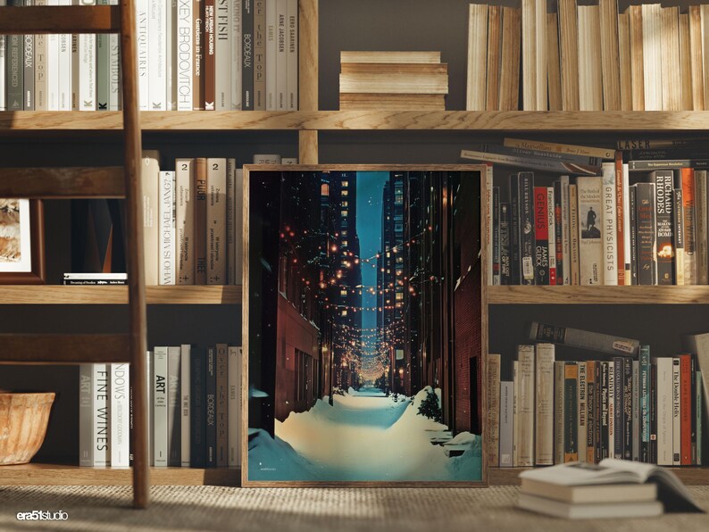 May include: A framed print of a snow-covered city alleyway at night, with string lights and tall buildings. The artwork is displayed in a wooden frame, set against a backdrop of bookshelves filled with books.