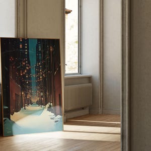 May include: A framed art print depicting a snow-covered street scene at night, illuminated by string lights. The artwork has a gold frame and is leaning against a wall near a window. The color palette includes blues, browns, and yellows.