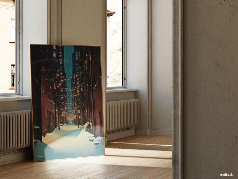 May include: A framed art print depicting a snow-covered street scene at night, illuminated by string lights. The artwork has a gold frame and is leaning against a wall near a window. The color palette includes blues, browns, and yellows.