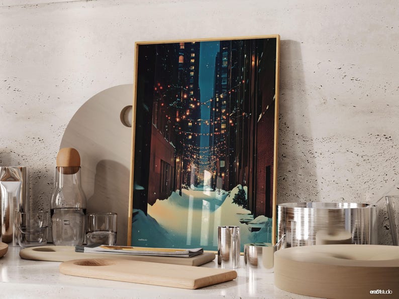May include: A framed art print depicts a winter alleyway scene with snow and string lights. The artwork has a gold frame and is displayed with wooden cutting boards, glassware, and metal containers. The color palette includes blues, browns, and yellows.