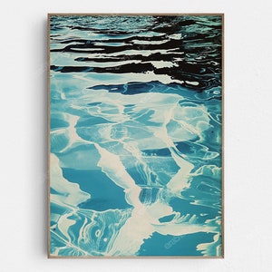 May include: Abstract art print featuring a blue and white water ripple pattern. The image is framed in a light wood frame.