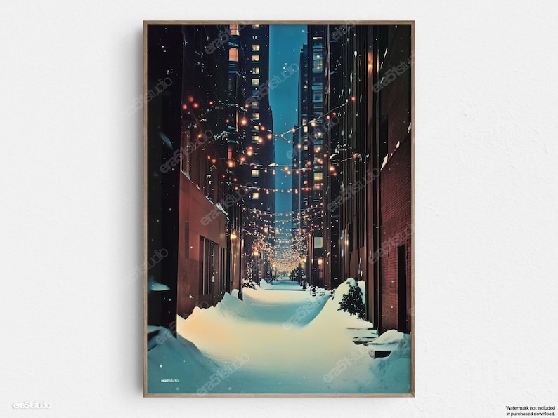 May include: A framed art print depicts a snow-covered alleyway between tall buildings at night. Strings of lights illuminate the scene, creating a warm glow against the cool blues and browns of the buildings and snow.