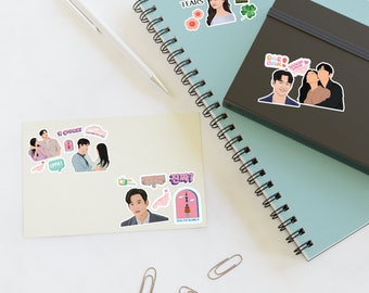 May include: A collection of stickers featuring characters and scenes from the Korean drama "Queen's Tears". The stickers are on a light blue notebook and a white surface. The stickers are colorful and feature a variety of characters and scenes from the show.