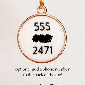 May include: Gold key chain with a round tag. The tag has a white background with black numbers 555 and 2471. The text "optional: add a phone number to the back of the tag!" is below the tag. The text "phone number will be the same color as the name" is below the first text.