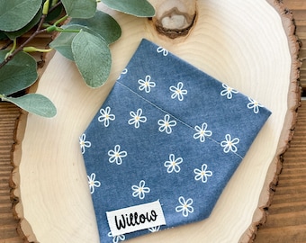May include: A blue bandana with a white daisy print and the name "Willow" on a white tag. The bandana is on a wooden slice.