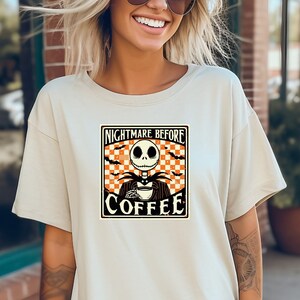 Pode incluir: Uma camiseta branca com um gr&aacute;fico de estilo vintage de Jack Skellington de O Estranho Mundo de Jack segurando uma x&iacute;cara de caf&eacute;. O gr&aacute;fico diz "Nightmare Before Coffee".