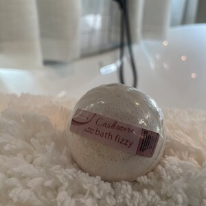May include: A white bath fizzy with a label that reads "Cashmere bath fizzy" and "Shea Butter".