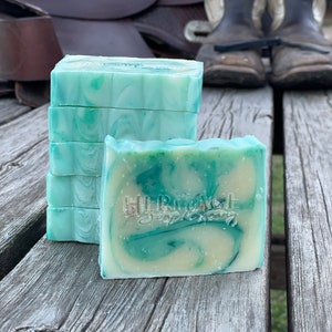 May include: Stack of six green and white swirl handmade soap bars with the text "HERITAGE Soap Company" on the bottom bar.
