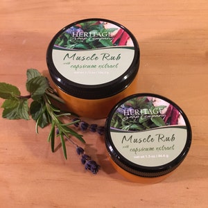 Può includere: Due barattoli di vetro ambrato di balsamo muscolare con tappi neri ed etichette bianche. Le etichette riportano "HERITAGE Soap Company" e "Muscle Rub with capsicum extract". Il barattolo più grande è etichettato "net wt 3.75 oz/100.3 g" e il barattolo più piccolo è etichettato "net wt 1.5 oz/44.4 g".