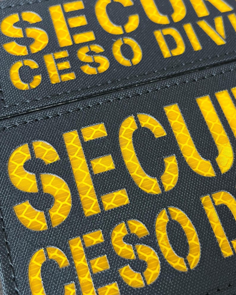 Peut inclure: Un &eacute;cusson rectangulaire noir avec des lettres r&eacute;fl&eacute;chissantes jaunes en gras. Le texte indique SECU et CESO DIVI dans une police de style pochoir. Les lettres jaunes pr&eacute;sentent une texture en nid d'abeille et l'&eacute;cusson est cousu en noir.