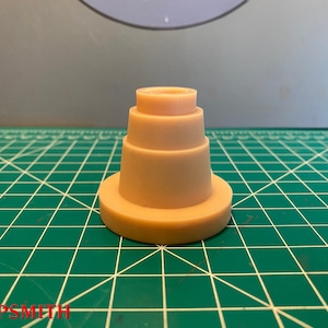 May include: A beige plastic tiered cake stand with four tiers. The stand is on a green cutting mat.