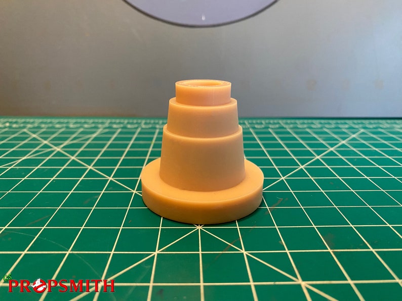 May include: A beige plastic tiered cake stand with four tiers. The stand is on a green cutting mat.