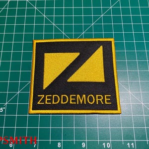 Peut inclure: Patch brodé noir et jaune avec une ligne diagonale et le texte "ZEDDEMORE".