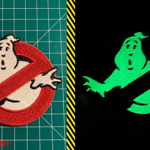 Op de afbeelding: Een geborduurde patch van het Ghostbusters-logo met een geest in het midden, in rood en wit. De patch gloeit in het donker groen.