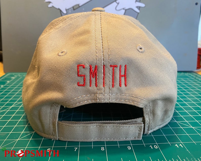 Op de afbeelding: Een beige baseballpet met een rood geborduurd "SMITH" op de achterkant.