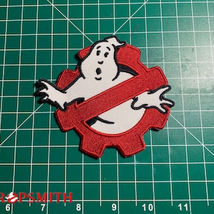 Może przedstawiać: Naszywka haftowana na czerwono i biało z logo Ghostbusters. Logo to czerwony symbol "no-ghost" z białym duchem w środku.