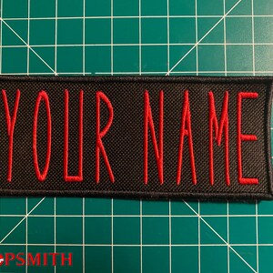 Pu&ograve; includere: Toppa ricamata nera con cuciture rosse. La toppa dice "YOUR NAME" in rosso.