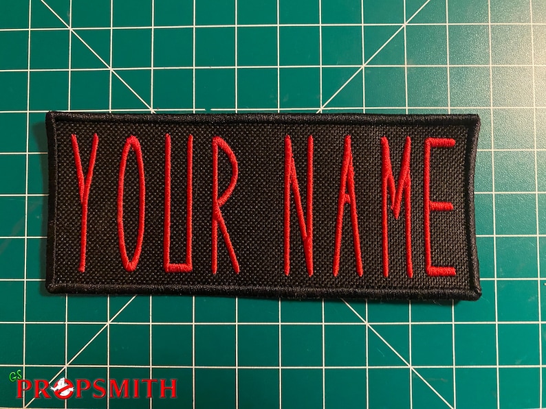 Pu&ograve; includere: Toppa ricamata nera con cuciture rosse. La toppa dice "YOUR NAME" in rosso.