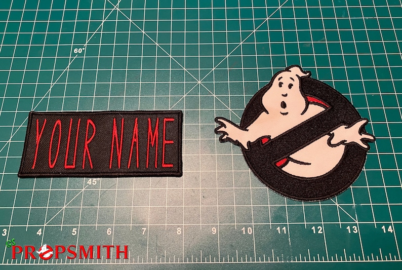 Op de afbeelding: Twee geborduurde patches, een zwarte met rode tekst die "YOUR NAME" zegt en de andere een witte geest met een zwarte cirkel en een rode streep.