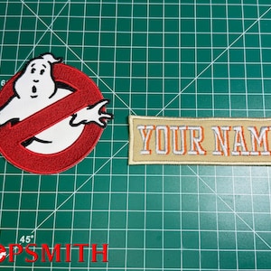 May include: A circular embroidered patch featuring a white ghost character inside a red circle with a diagonal slash, alongside a rectangular tan embroidered patch with the orange and white text YOUR NAME stitched in a block font style.