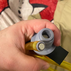 May include: Close-up of a yellow plastic tube connected to a gray plastic connector. The connector has a small hole in the center. The tube is bent into a circle.